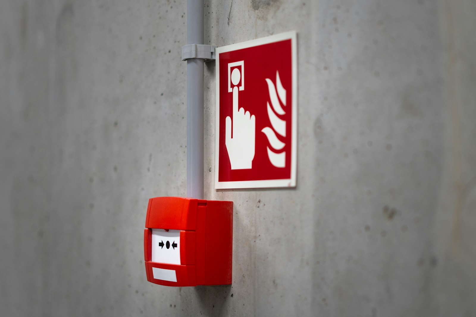 Red manual fire alarm call point mounted beside its pictogram sign